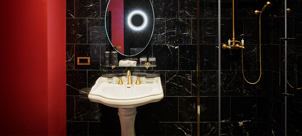 Deluxe Room: Schwarzes Marmorbad mit goldenen Amaturen, Retrowaschbecken und Spiegel mit Schminklicht