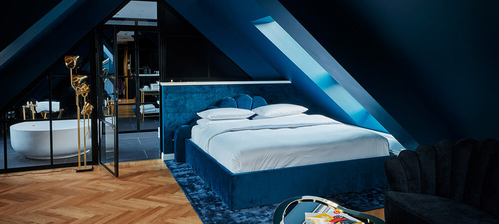 Maison Suite: Kingsize Bett auf blauem Teppich unter dem Dachfenster